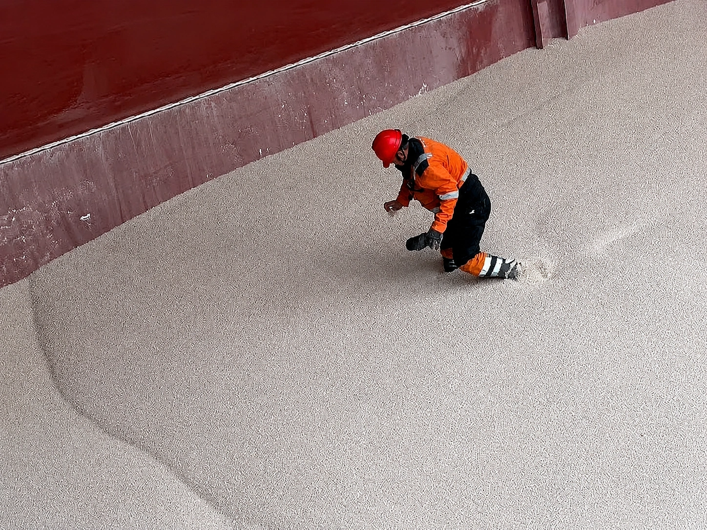 Worker inspecting gray granular cargo inside a vessel hold