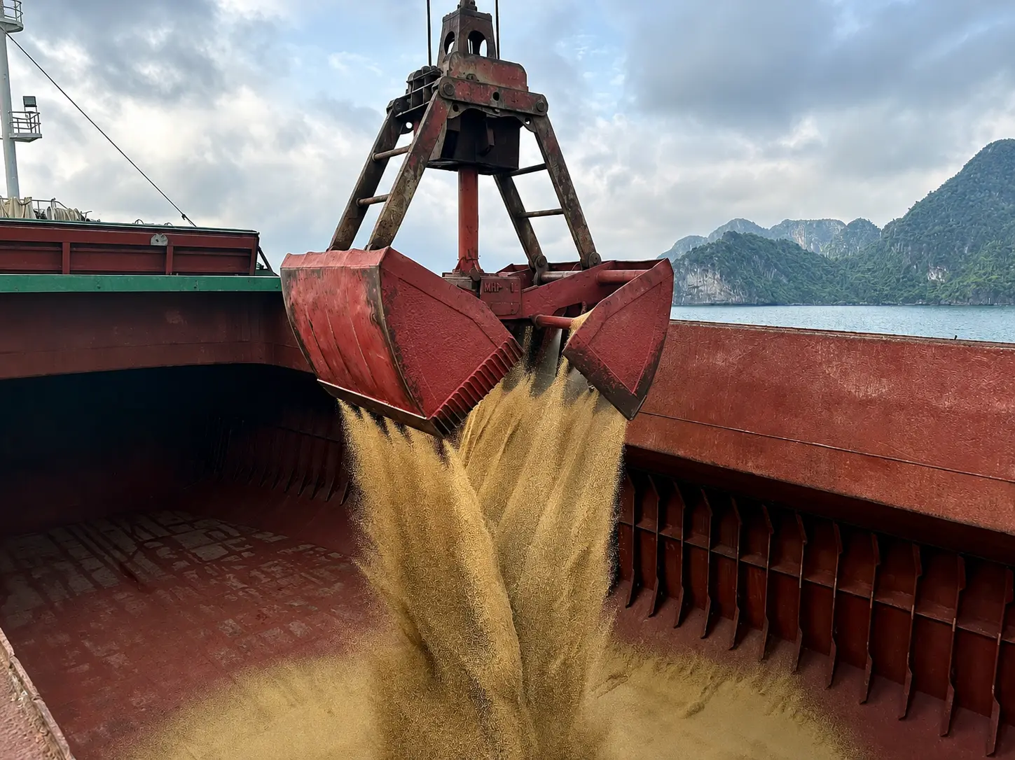 Grab bucket unloading yellow granular fertiliser cargo into a vessel hold